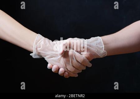 Handshake in medical gloves on black background. Partial view. Stock Photo