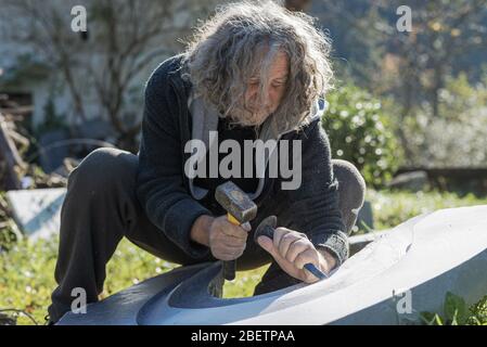 Tired senior artist carving curves in marble stone using mallet and chisel. Stock Photo