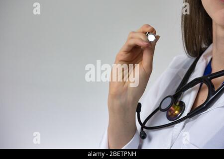 Medical professional with pen light isolated on grey background. Stethoscope and white coat visible. Room for type and copy Stock Photo