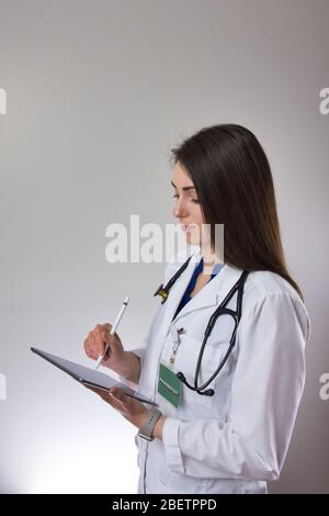Lady medical professional making note on tablet for patient charting. Isolated portrait on grey background Stock Photo