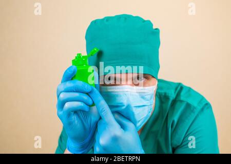 Green antiseptic bottle in Doctor hands in green suit and blue mask gloves with on yellow background. It is important to use antiseptic on your hands  Stock Photo