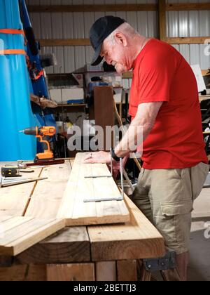 Active Adult Senior Man in workshop working on building a shelf. Stock Photo