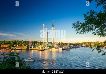 Djurgarden island and Tivoli carousel amusement attractions Grona Lund (Luna Park) with green forest and blue sky background and water of Lake Malaren Stock Photo