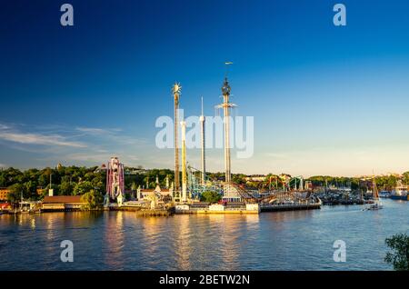 Djurgarden island and Tivoli carousel amusement attractions Grona Lund (Luna Park) with green forest and blue sky background and water of Lake Malaren Stock Photo