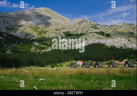 Small houses and grass meadow near Negushi village in front of rocks mountains, Montenegro Stock Photo