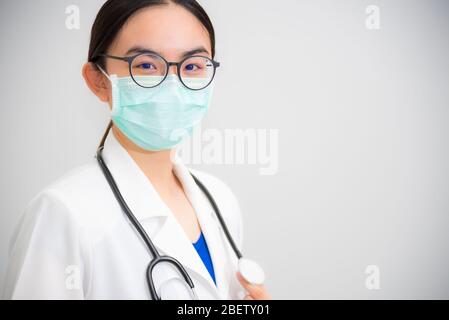 Studio portrait beautiful Asian young woman doctor with stethoscope in white uniform wear glasses and green mask to protect Corona Virus for health lo Stock Photo