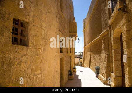 Narrow stone streets with yellow buildings in the old medieval Cittadella tower castle, also known as Citadel, Castello in the Victoria Rabat town, Go Stock Photo