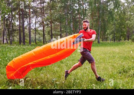 A young man inflates a lamzac with air. A man inflates an air sofa. on the background of the forest Stock Photo