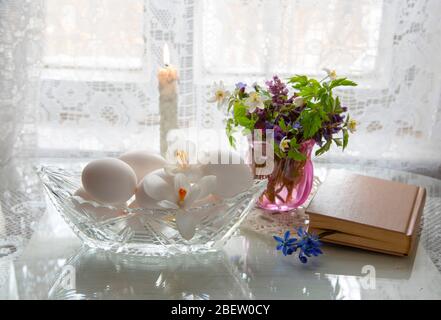 Spring flowers in a glass and white eggs in a crystal vase on a white background. Stock Photo