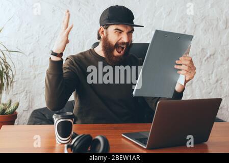 Photo of angry bearded man screaming in office and looking at paper work Stock Photo