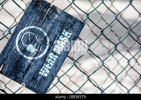 Old cracked rectangular wooden plate on the old green mesh fence with the inscription Wear Mask. Stock Photo