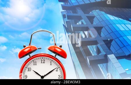 Red alarm clock on a modern townhouse and blue sky background. The concept illustration. Stock Photo