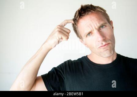 Casual young man in black T-shirt scratching his head looking at the camera with a pensive expression Stock Photo