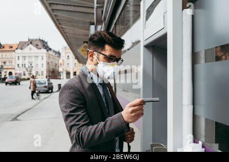 Business man with protective face mask using street ATM machine. Stock Photo