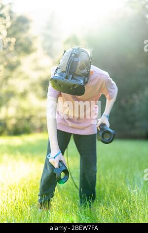 Tween playing virtual reality game in green field with VR goggles on Stock Photo