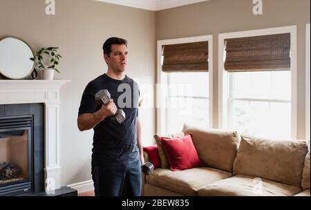 Fit man exercising at home with hand weights in his living room. Stock Photo
