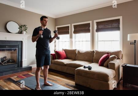 Fit man exercising at home with hand weights in his living room. Stock Photo
