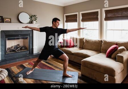 Fit man doing warrior yoga pose at home in his living room. Stock Photo