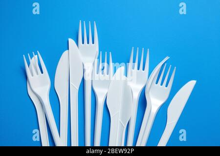 White plastic knives and forks. Disposable plastic tableware on blue background, top view Stock Photo