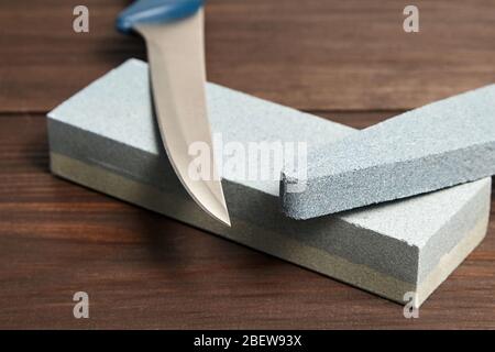Grindstones. Two whetstones and steel knife blade. Oval and rectangular double layer sharpening stone on wooden table background Stock Photo