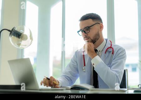 Man doctor is thinking about the result of an examination of his patients. Emotion with the young man doctor being exhausted. Pensive nurse reading so Stock Photo