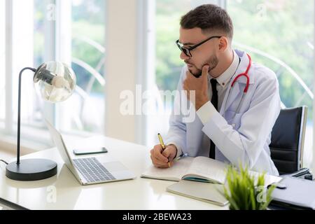 Man doctor is thinking about the result of an examination of his patients. Emotion with the young man doctor being exhausted. Pensive nurse reading so Stock Photo