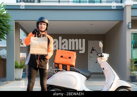 Delivery Asian man wearing orange uniform and ready to send delivering Food bag in front of customer houes with case box on scooter, express food deli Stock Photo