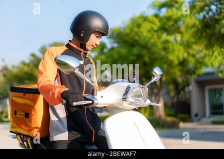 Asian man courier checking customer location in map in smartphone on scooter delivering food in town streets with a hot food delivery from take aways Stock Photo