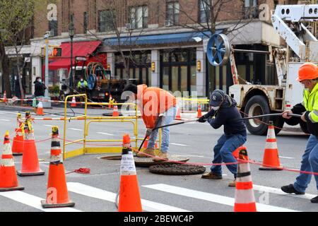 Workers pulling telecommunication cable from a manhole in Manhattan, New York, NY. Stock Photo