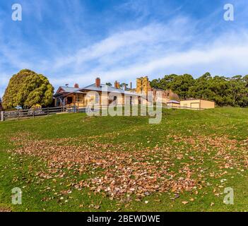 Foreground grassy paddock with fallen leaves leading to the Canadian Cottage Port Arthur Historical site in Tasmania Australia. Stock Photo
