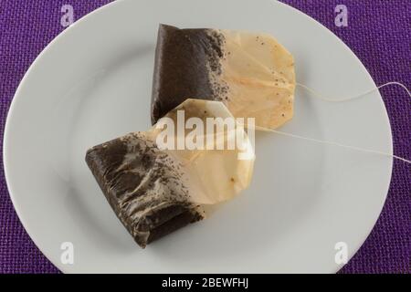 Two used black tea teabags on white plate on purple tablecloth after making iced tea Stock Photo