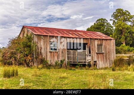 An abandoned weatherboard and corrugated iron, pioneer barn house or shed on a hillside along the the Tasmanian east coast in Australia. Stock Photo