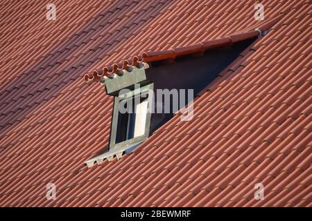 Small green dormer window in a sea of red tiles on the roof of a building in Prague in the winter sunshine Stock Photo