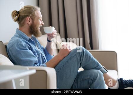 Happy relaxed young man lounge on comfortable sofa drinking tea. Stock Photo