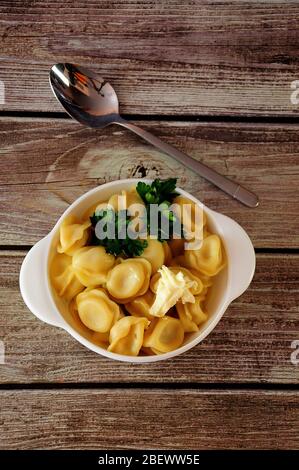 A plate with freshly cooked dumplings with herbs and butter stand on a wooden table, next to a spoon. Close-up. Stock Photo