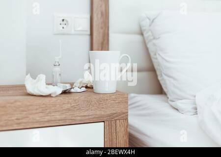 Medicines, pills, nose drops, tissues and hot drink cup on bedside table in modern apartments. Being sick, unwell, flu, illness symptoms. Coronavirus Stock Photo