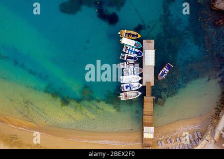 Aerial of a peer with boats and blue ocean water. Boat peer shot from a drone in mediterranean sea in Greece, Corfu Stock Photo