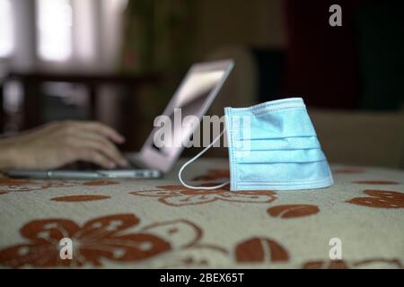 Work at home during coronavirus outbreak. Focus on face mask with computer laptop and home background. Work from home concept. Stock Photo