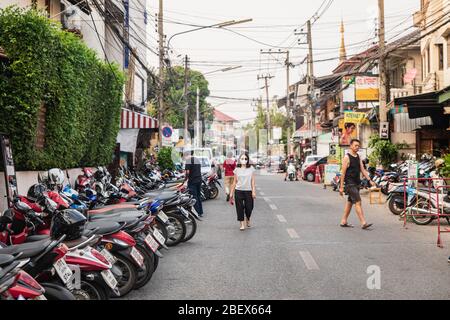 Chianf Mai, Thailand - February 9, 2020: Woman in black mask walking on street full of motorbikes in touristic Chiang Mai town in Northern Thailand Stock Photo