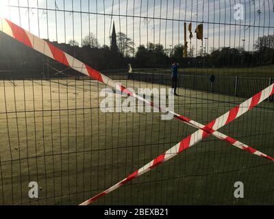 Glasgow, UK, 16 April 2020. A man exercises early morning in Queen's Park, beside fences and tape showing the restrictions in place on a basketball/football pitch, to ensure correct social distancing of the public and to prevent gatherings of people, during the current Coronavirus COVID-19 pandemic health crisis.  Photo credit: Jeremy Sutton-Hibbert/ Alamy Live News. Stock Photo