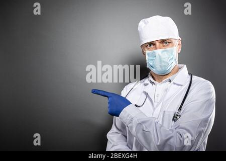 Doctor in white uniform and protective medial mask pointing left Stock Photo
