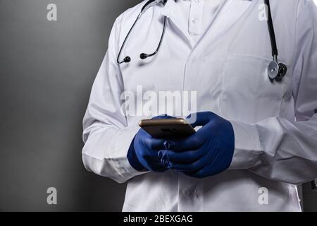 Doctor in white uniform and protective gloves using smart phone Stock Photo