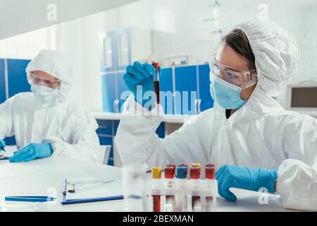 biochemist holding test tube with blood sample near colleague in laboratory Stock Photo