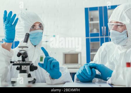 two biochemists in hazmat suits talking in laboratory near microscope Stock Photo