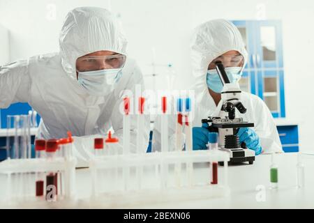 biochemist working with microscope near colleague looking at test tubes in lab Stock Photo