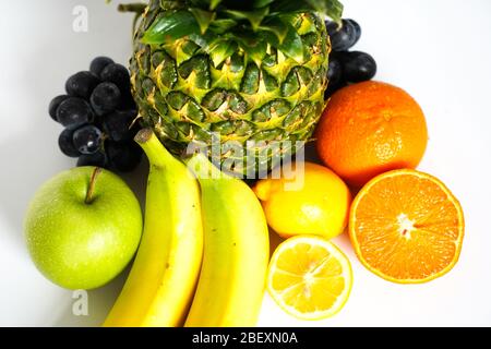 A selection of tropical fruit against a plain white background, including a whole pineapple, green apple, banana, orange, sliced lemon and a bunch of Stock Photo