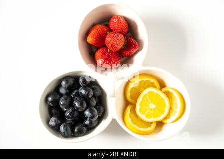 A serving dish with sliced lemons, strawberries and black grapes in each segment Stock Photo