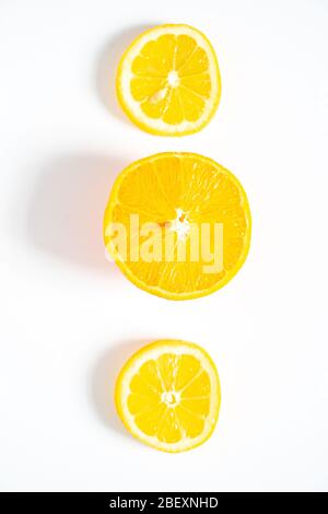 Two slices of lemon and one slice of orange laid out in a row against a plain white background Stock Photo