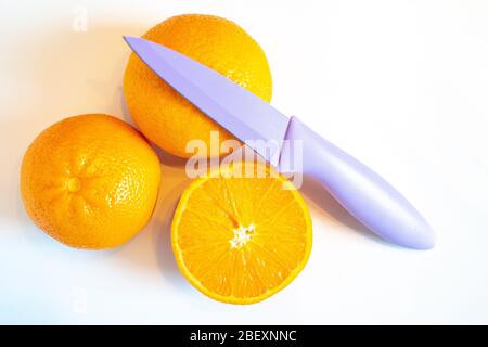 Three halves of orange with a sharp knife on a plain white background Stock Photo