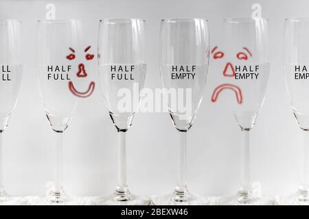 Six wine glasses, half full with drawn sad and happy faces in background depicting concept of glass half full, or glass half empty. Stock Photo